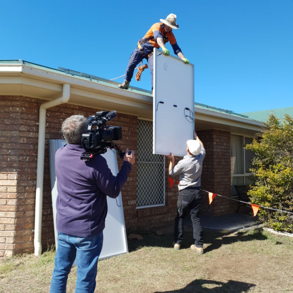 Camera man filming installer lifting solar panel to roof